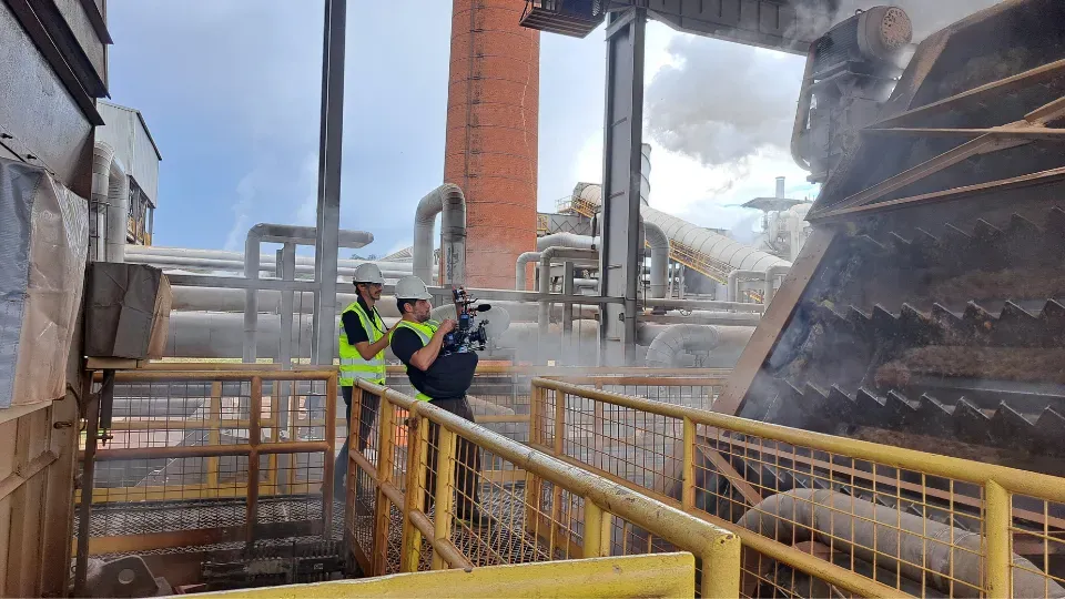 Two cameramen filming a machine in a factory