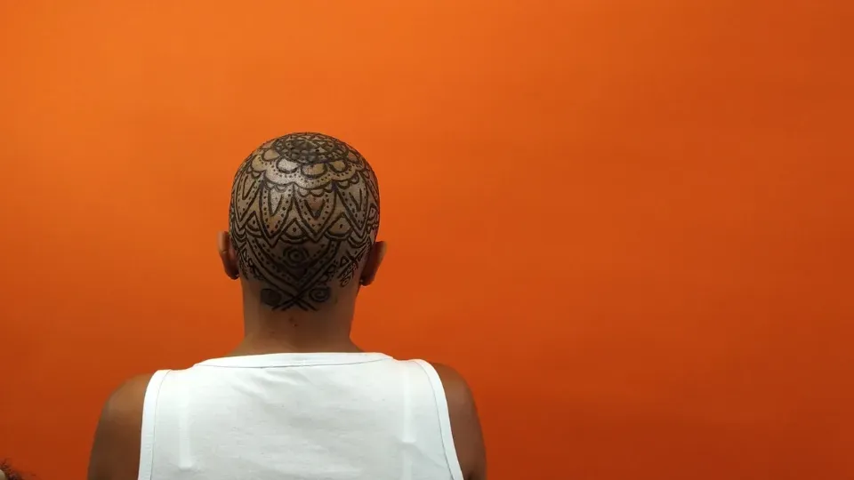 dark-skinned person sitting with his back, with a tattoo on his scalp