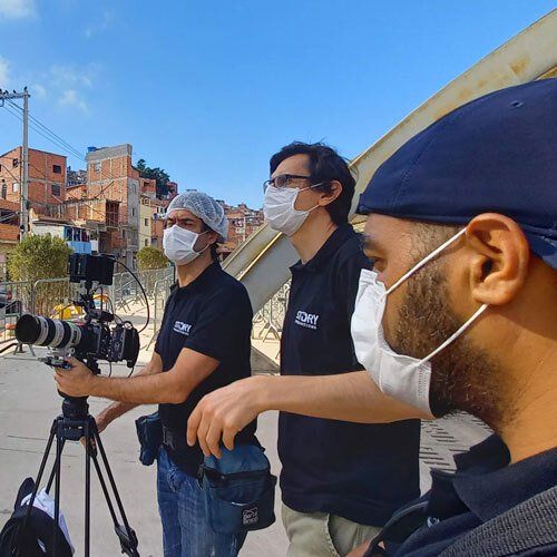 Three men wearing face masks are standing in front of a camera.