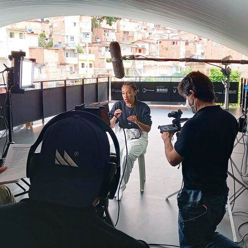 A man is taking a picture of a woman sitting in front of a camera.