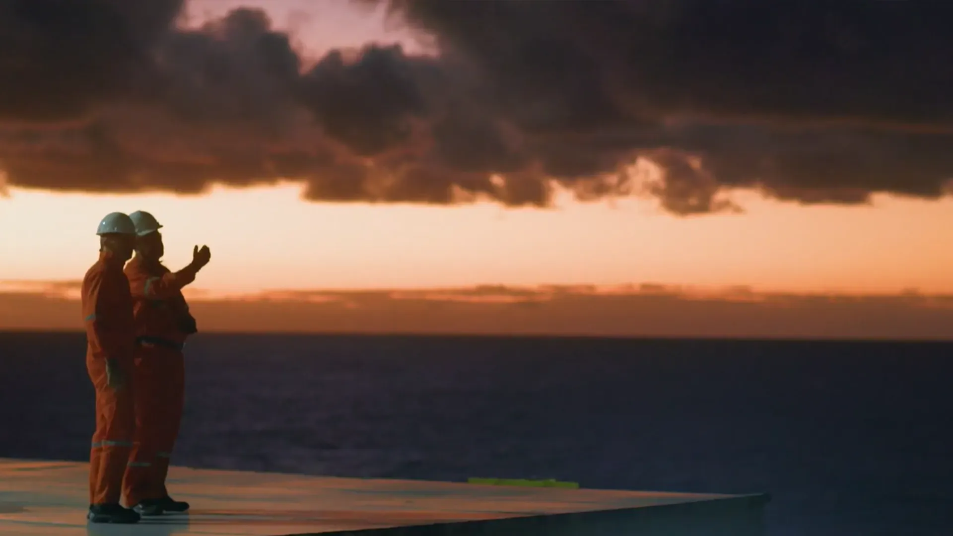Two men are standing on a platform overlooking the ocean at sunset.