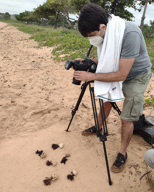 A man wearing a mask is taking a picture on the beach