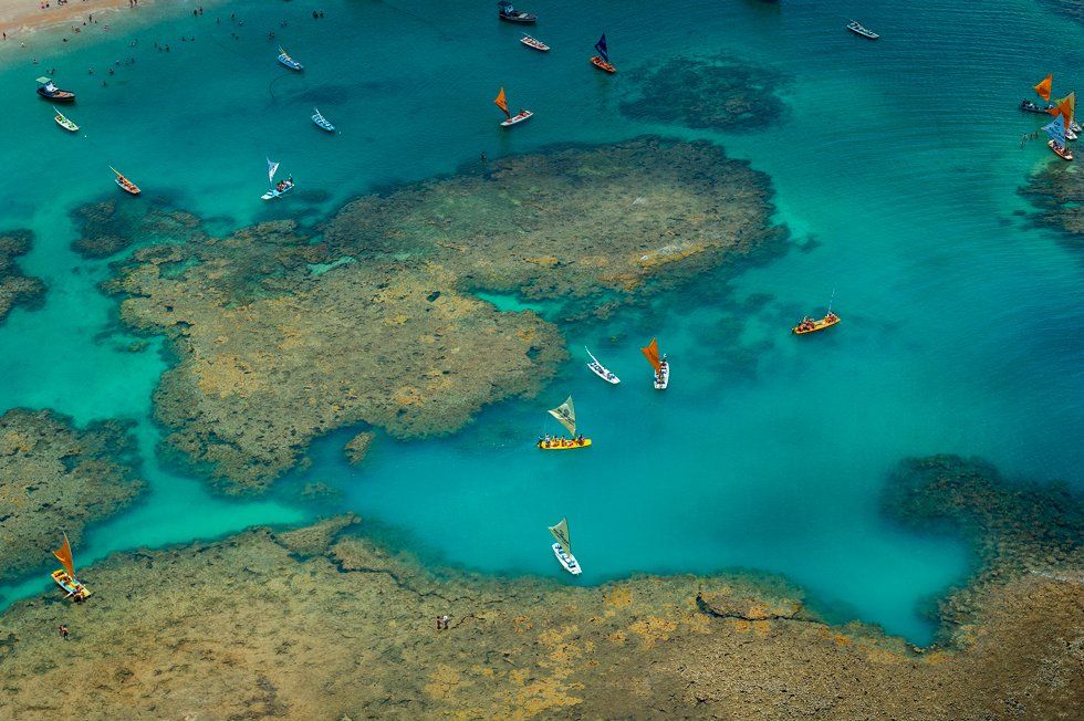 An aerial view of a coral reef in the ocean with boats in the water.