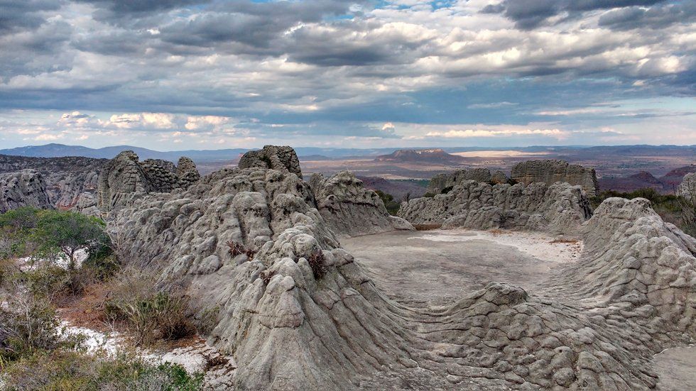A large rock formation in the middle of a desert with a cloudy sky in the background.