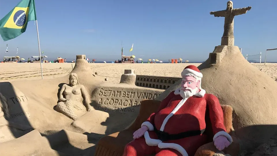 Santa claus is sitting in front of a sand sculpture on the beach