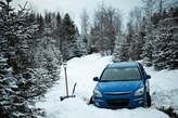 A blue car is stuck in the snow on a snowy road.