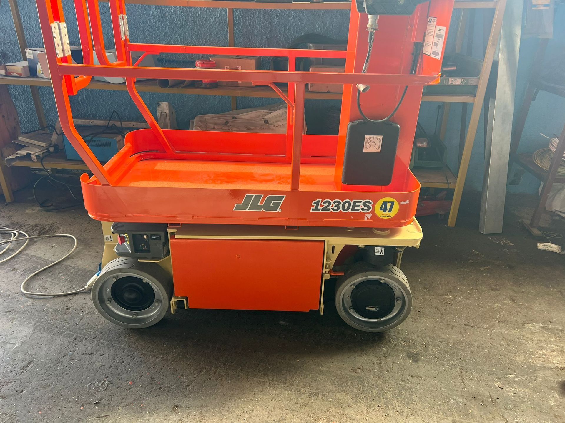 Piattaforma aerea JLG arancione. La piattaforma è dotata di piattaforma, parapetti di sicurezza e quattro pneumatici neri. All'interno di un garage.