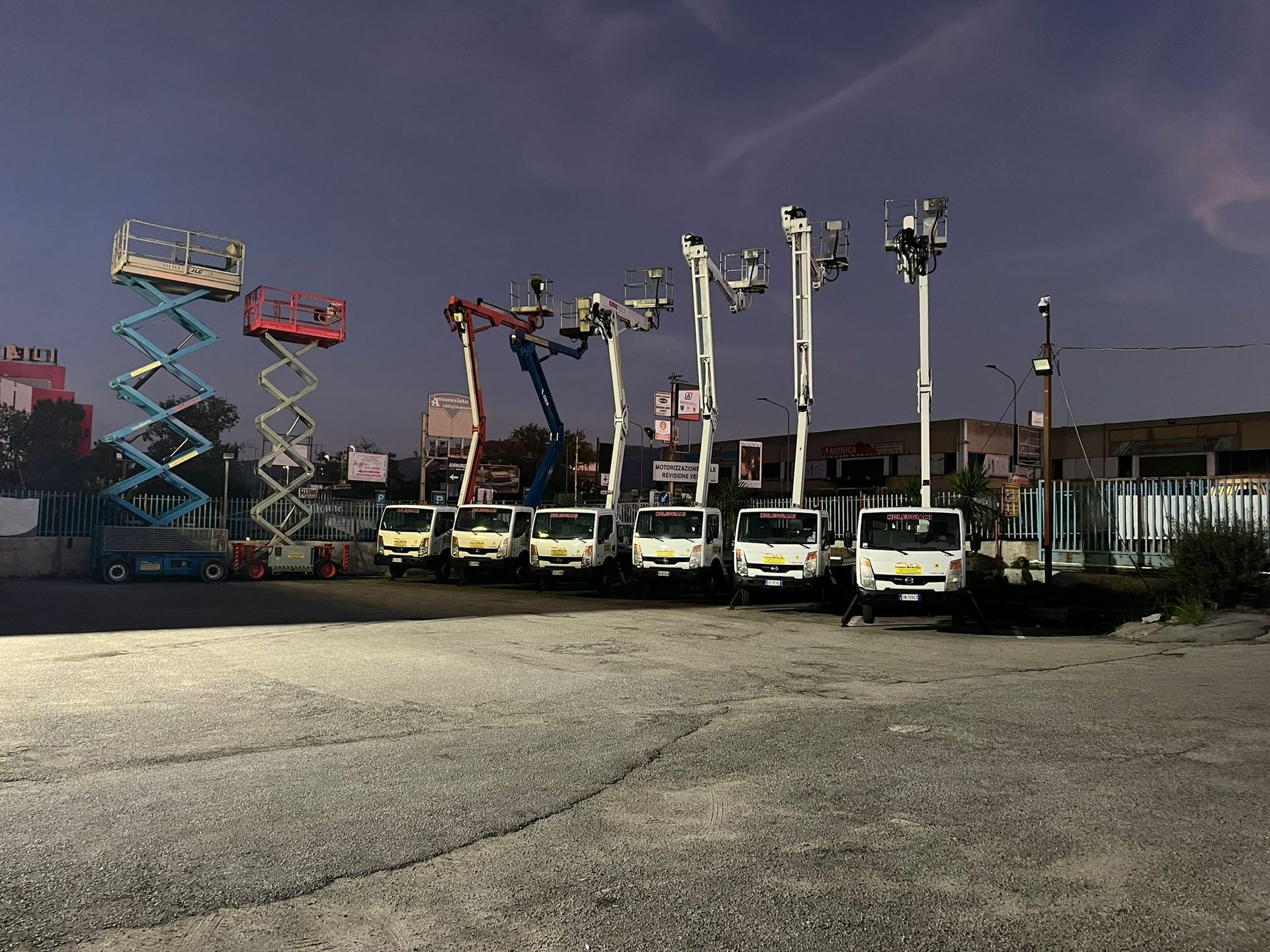 Carrelli elevatori aerei e una piattaforma aerea a forbice parcheggiati in un parcheggio al tramonto.