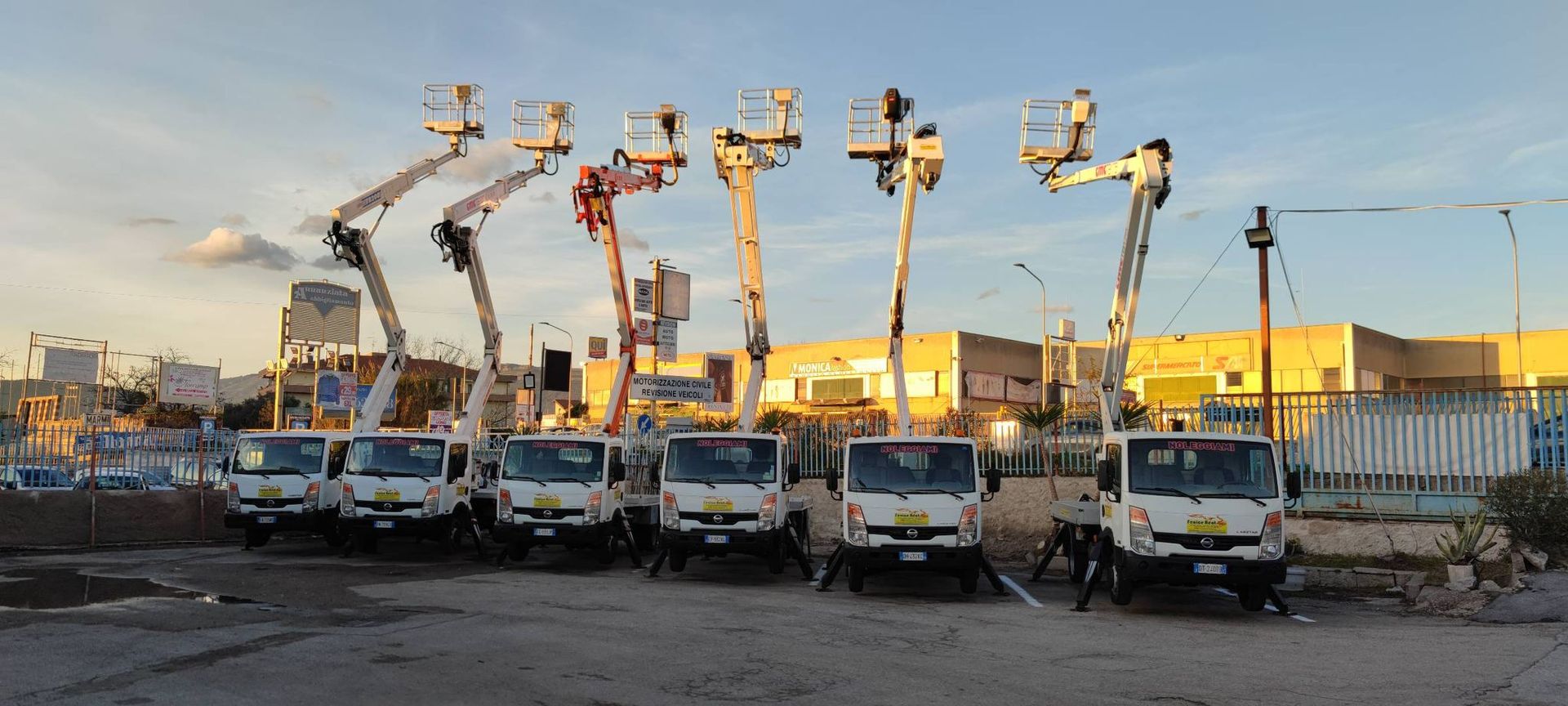 Una fila di camion bianchi con piattaforme aeree parcheggiati in un parcheggio all'aperto durante il giorno.