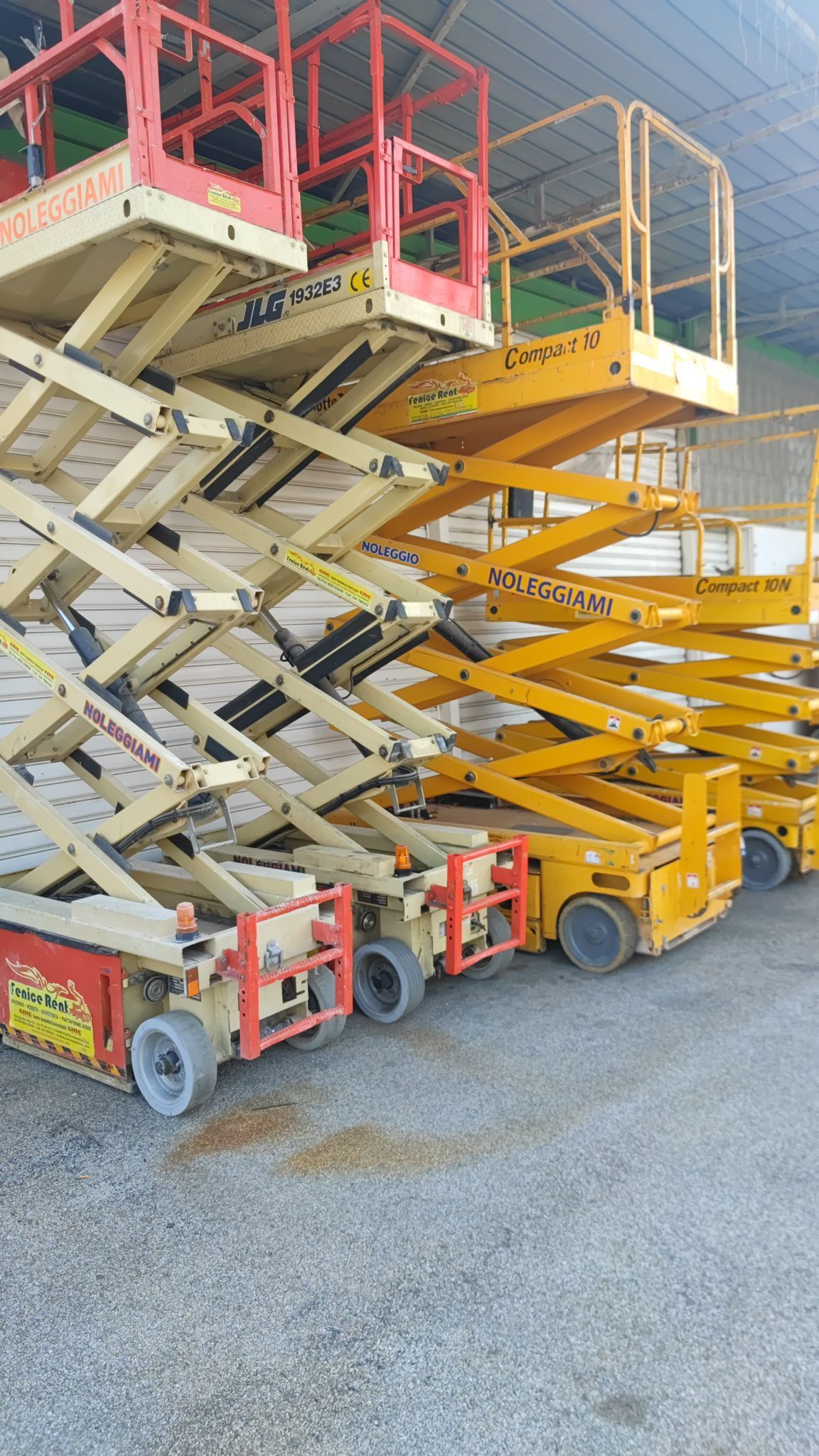 Diversi sollevatori a forbice gialli e rossi parcheggiati sul cemento.