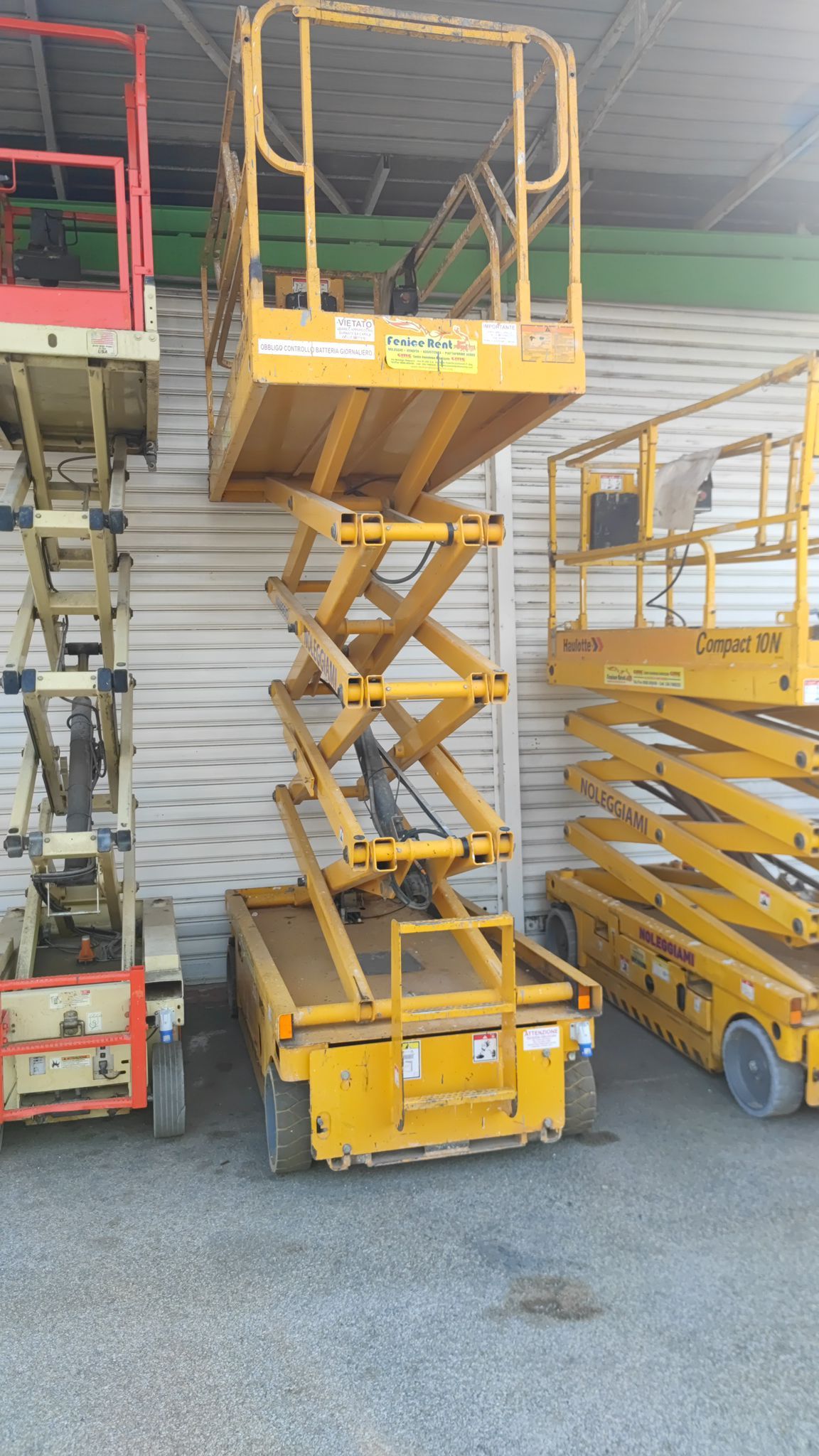 Piattaforma aerea gialla, elevata, parcheggiata accanto ad altre due.