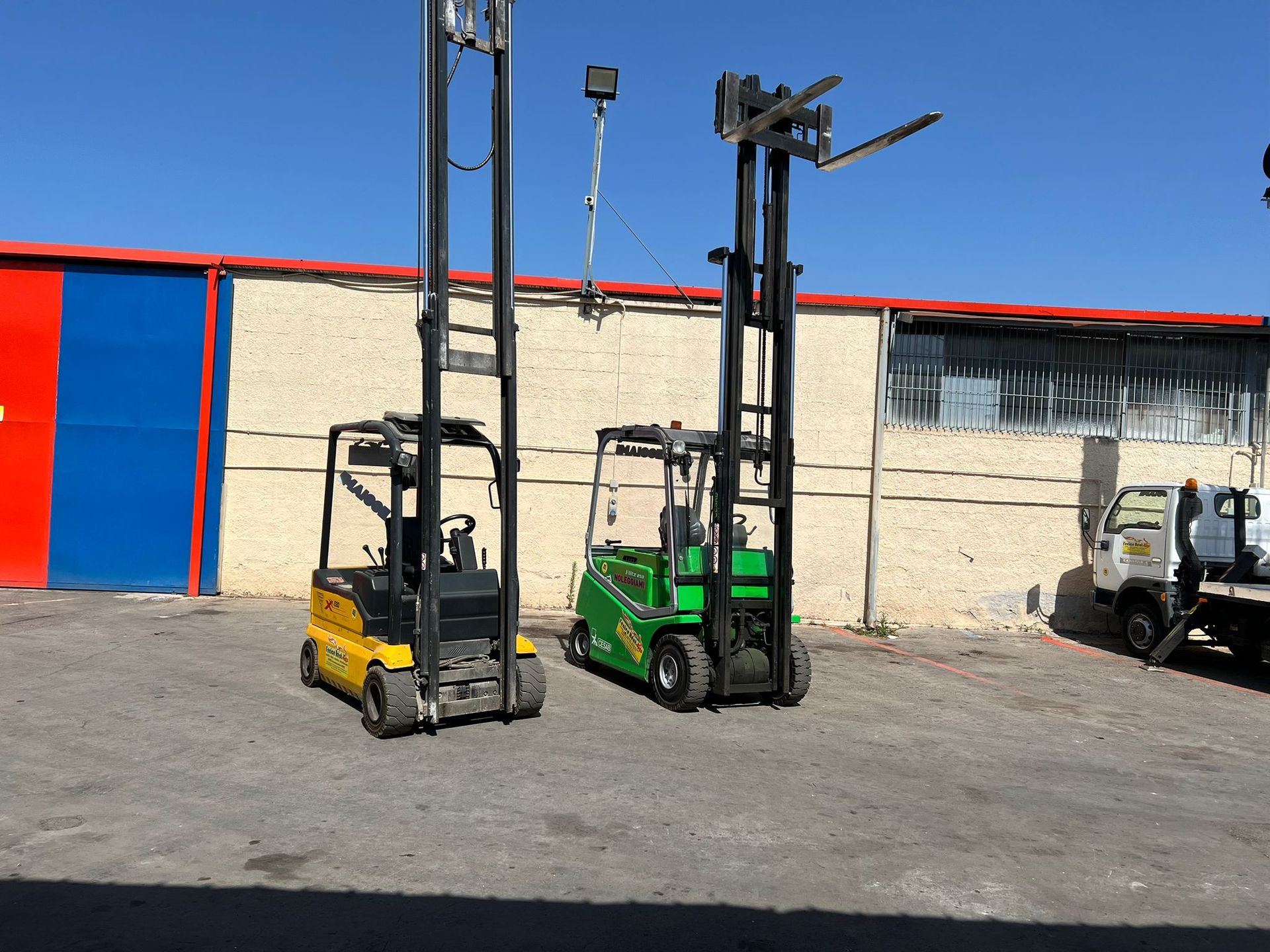 Due carrelli elevatori, uno giallo e uno verde, parcheggiati fuori da un edificio.