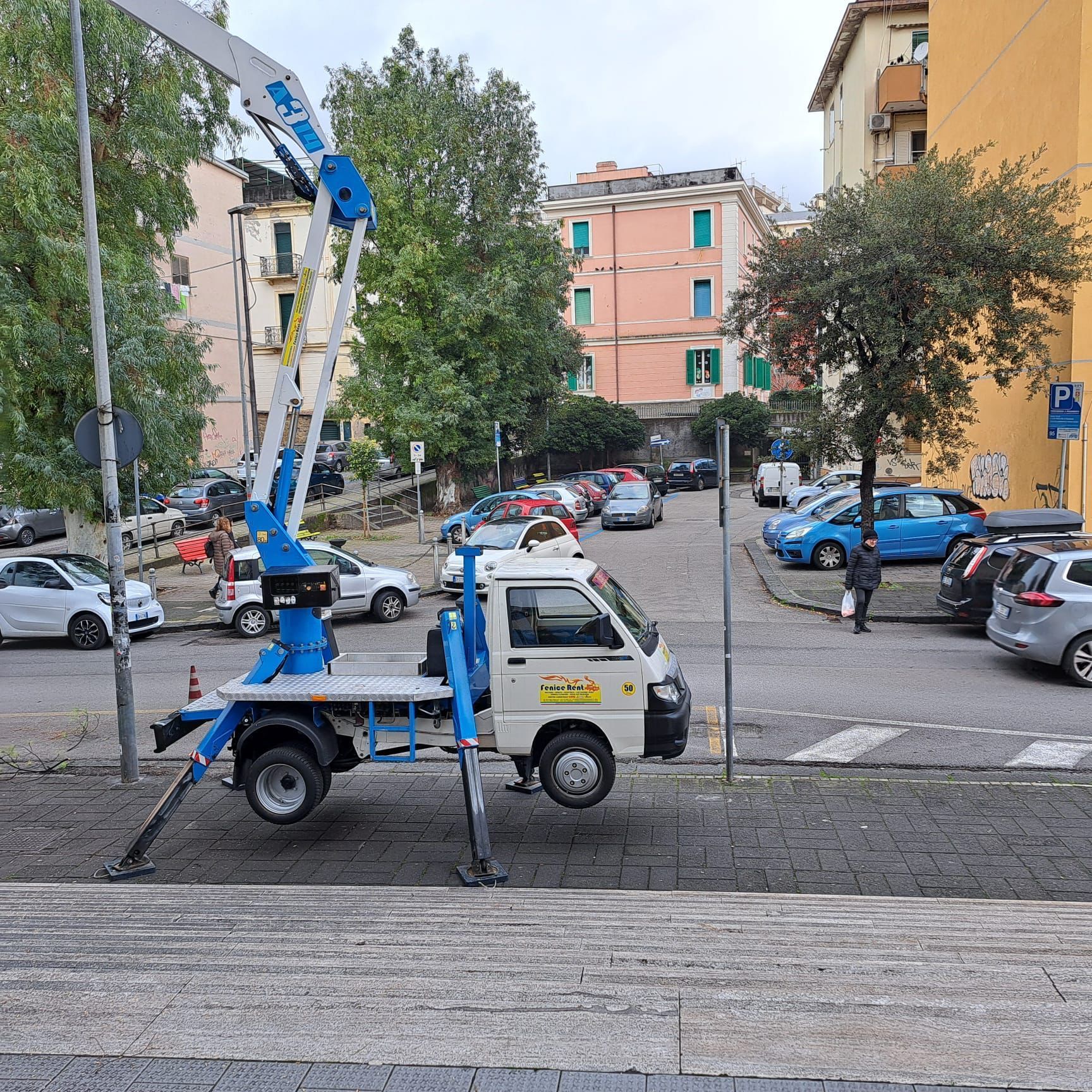 Un piccolo camion con una piattaforma aerea è parcheggiato su una strada vicino agli edifici.