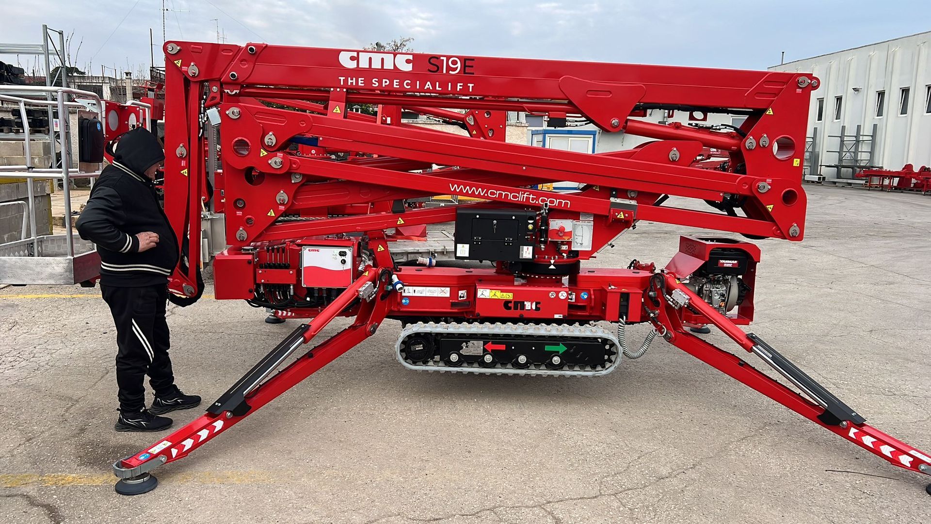 Uomo che ispeziona un ascensore rosso su binari, con gli stabilizzatori estesi.