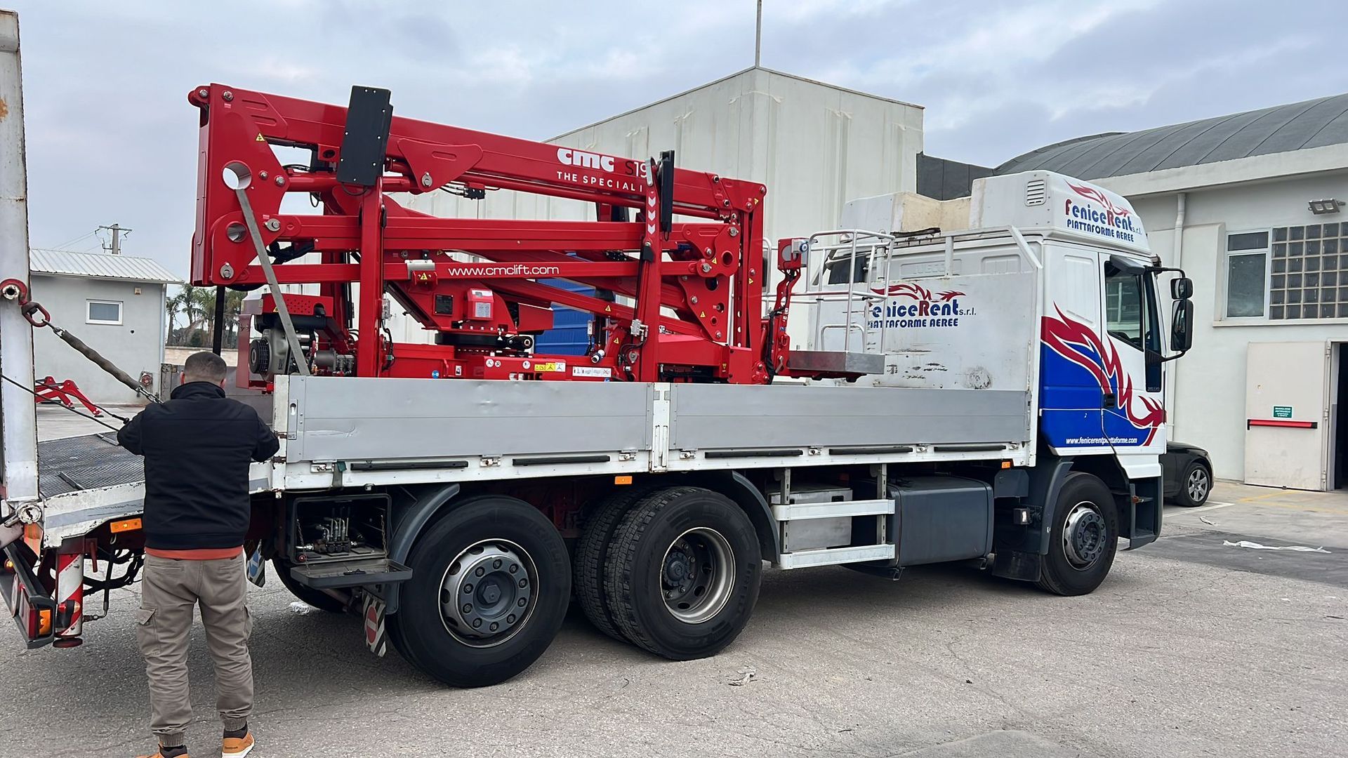 Camion con macchinari rossi, cabina bianca e blu, un uomo è in piedi vicino al camion.