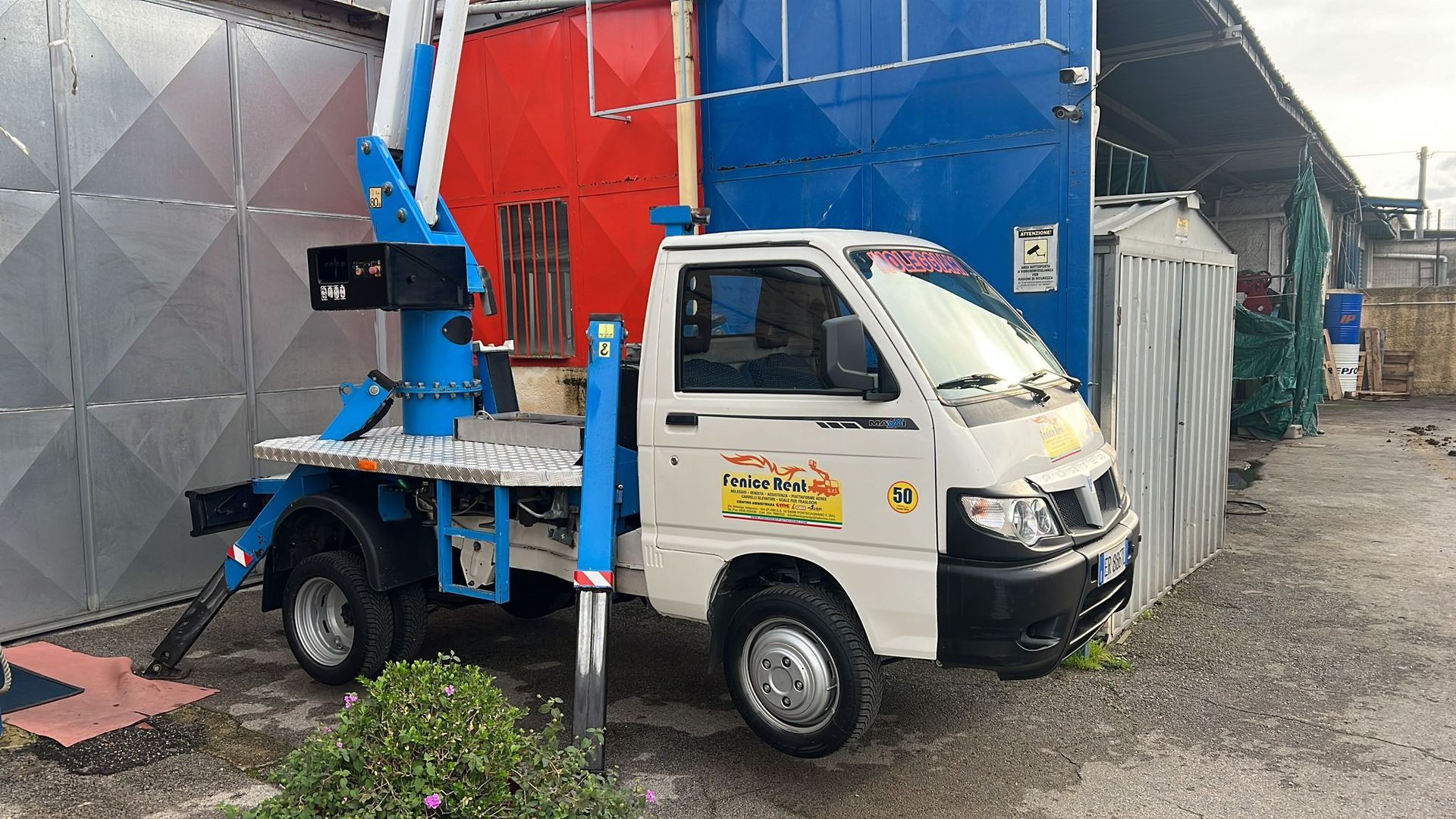 Un camion bianco con gru blu parcheggiato vicino a un edificio rosso e blu.