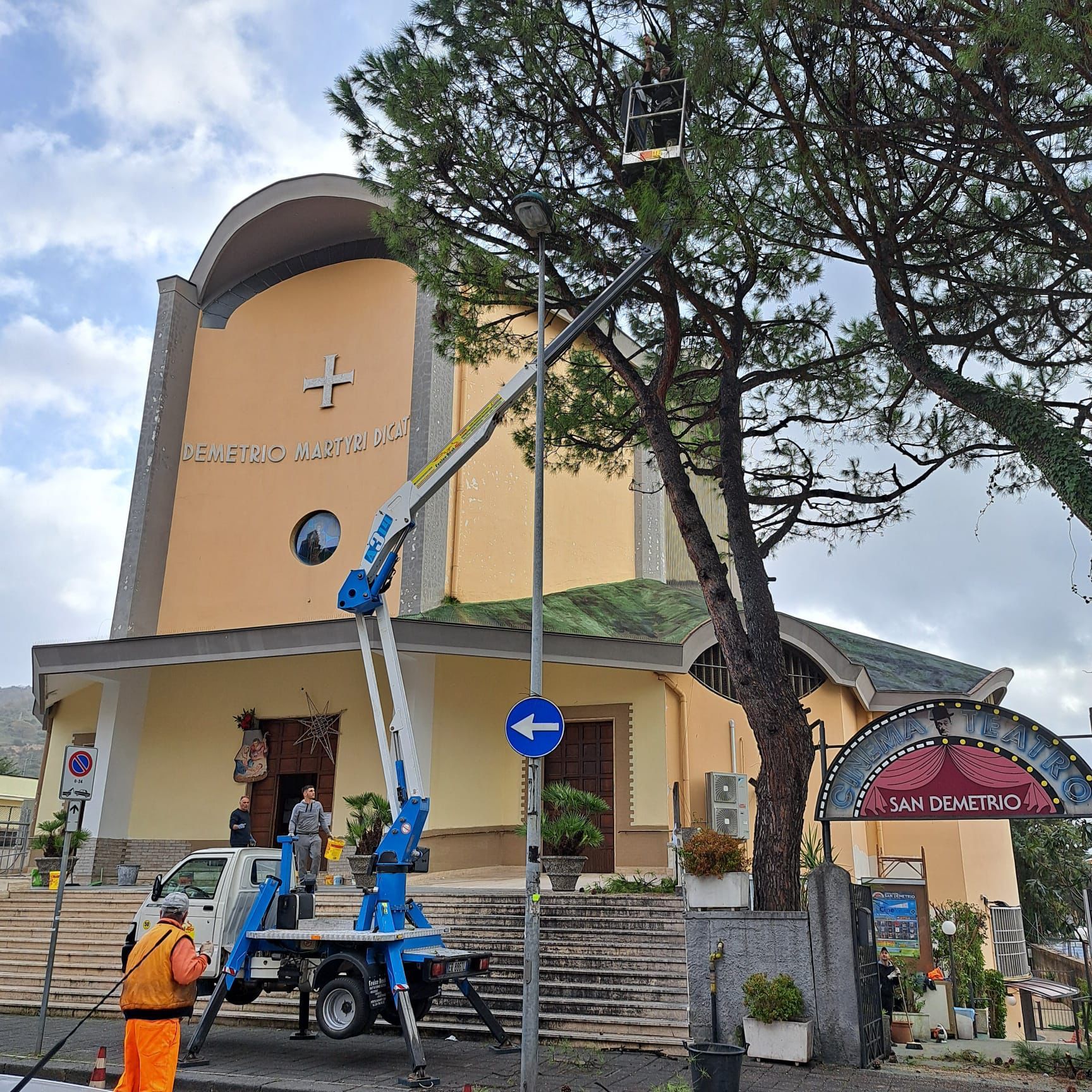 Esterno della chiesa con un albero che viene potato da un ascensore; operaio con giubbotto di sicurezza; Italia.