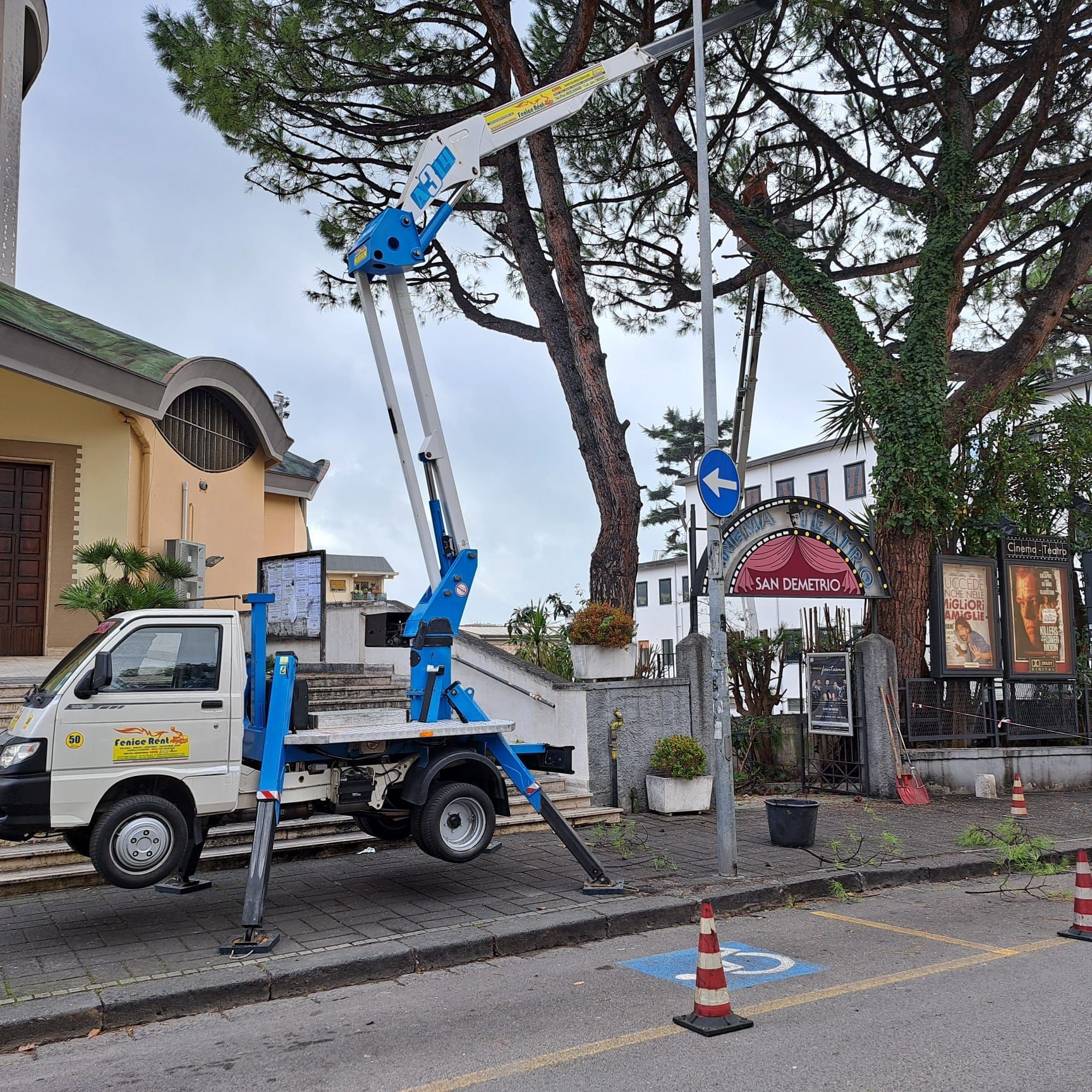 Un carrello elevatore blu con braccio esteso accanto a una chiesa e a un ristorante.