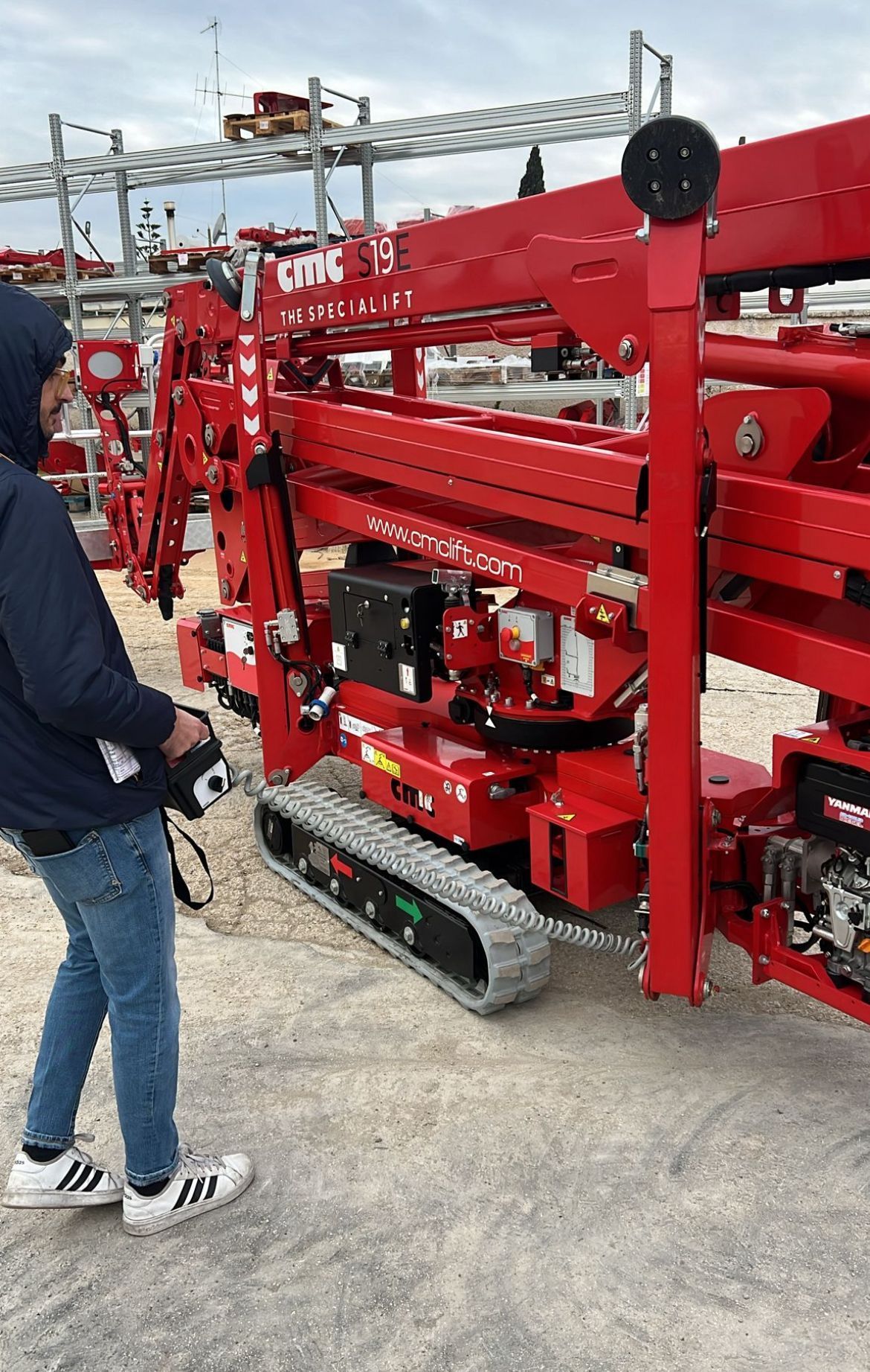 Persona che aziona un elevatore rosso su rotaia con un telecomando, all'aperto in una giornata nuvolosa.