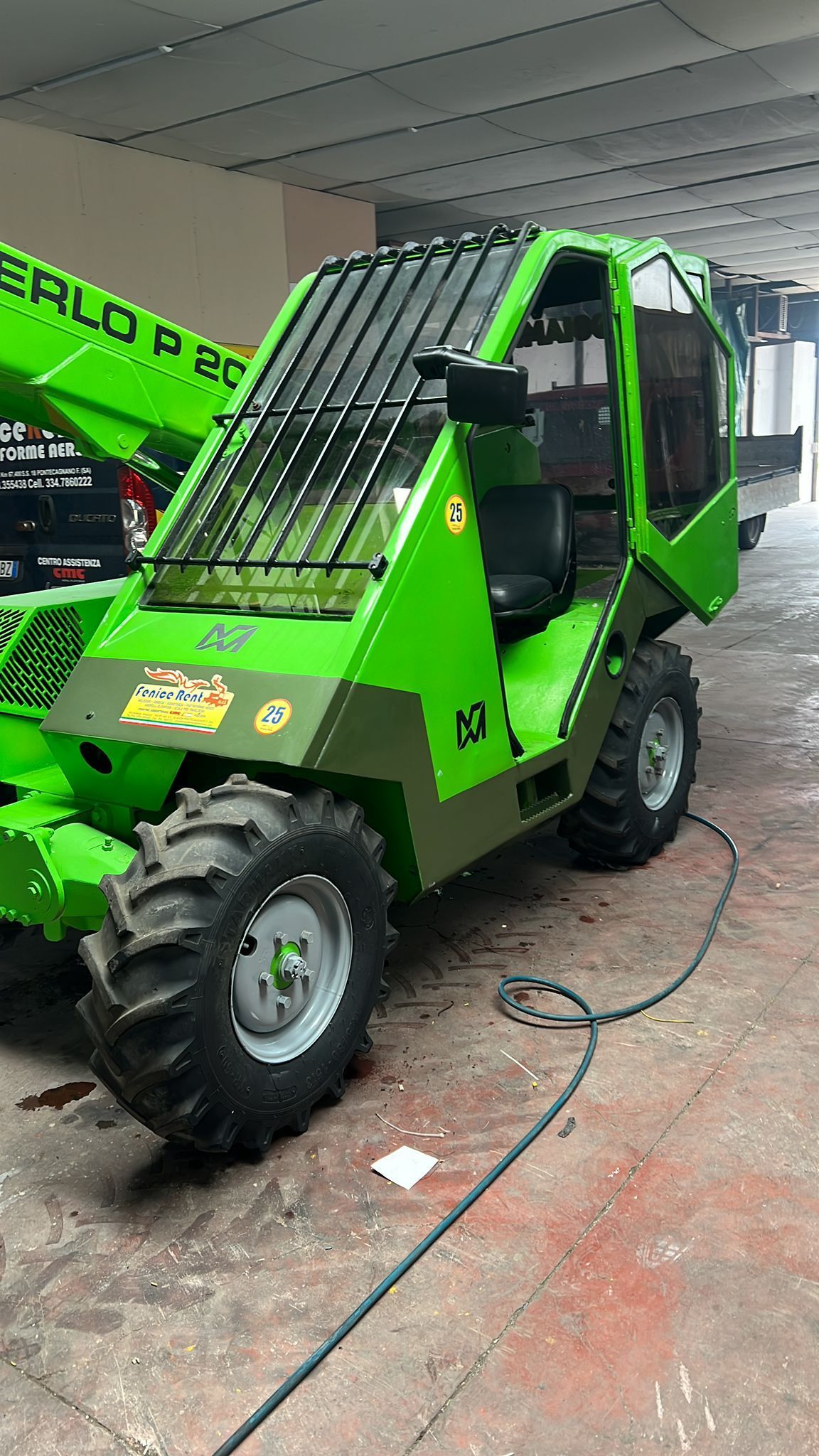 Sollevatore telescopico Merlo verde in un magazzino, con pneumatici neri e tetto in vetro.