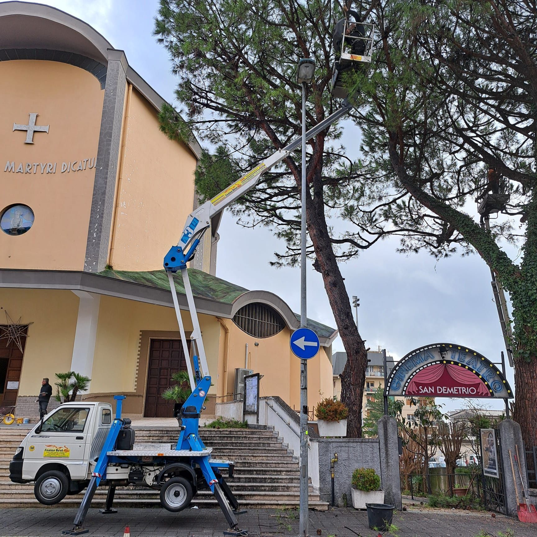 Una chiesa e un camion con gru al lavoro su un lampione di fronte.