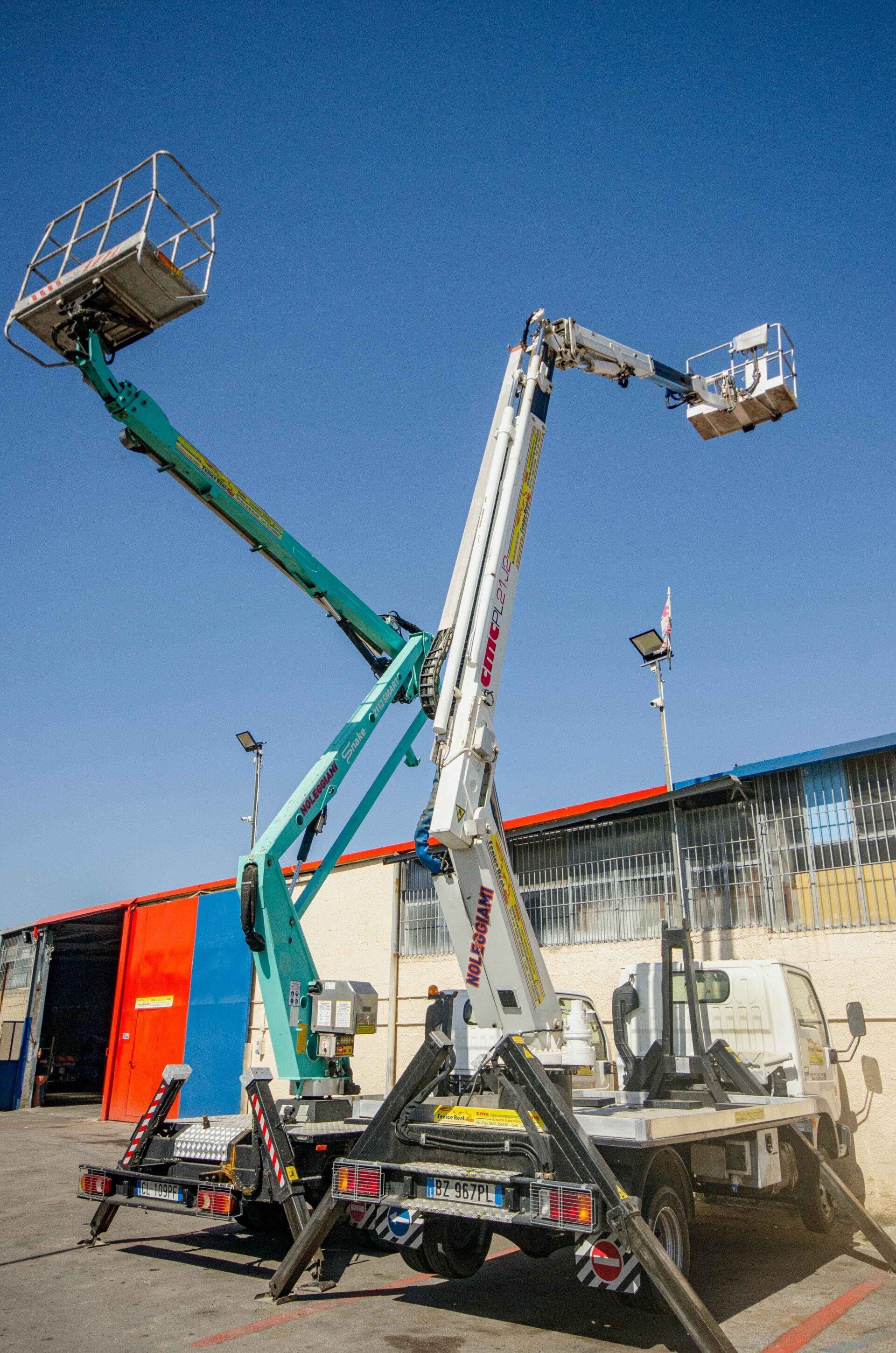 Due piattaforme aeree su un camion, una verde e una bianca, si stagliano contro un cielo blu.