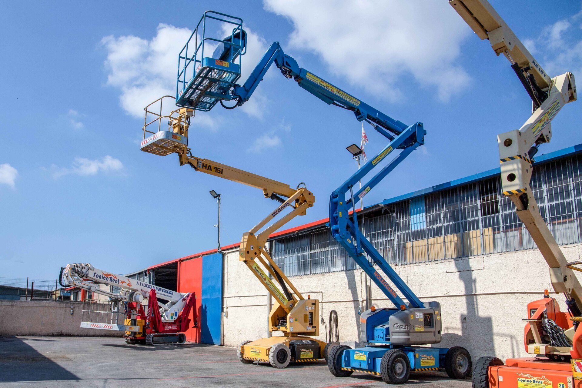 Piattaforma aerea blu e gialla estesa vicino a un edificio con uno sfondo di cielo azzurro.