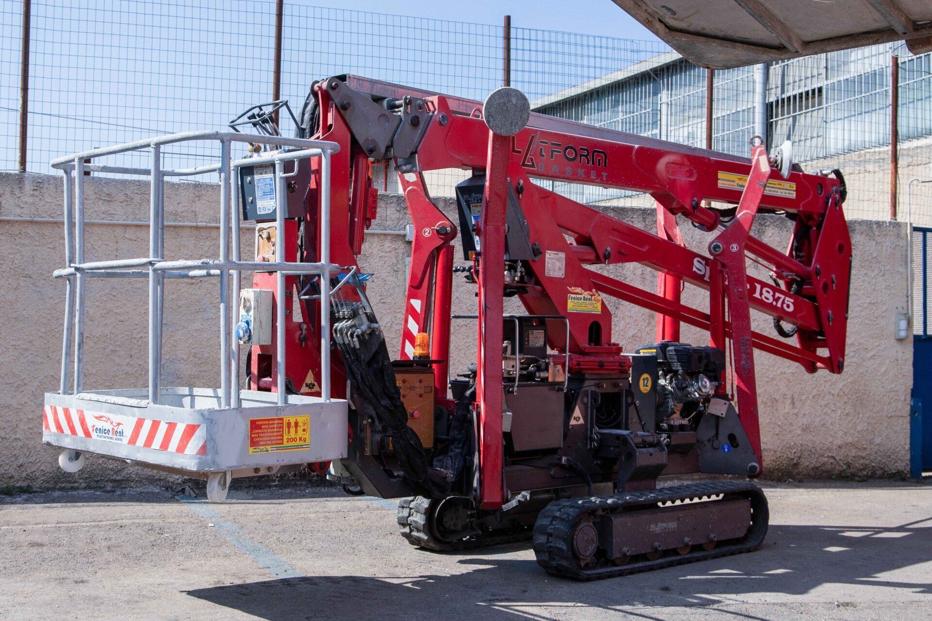 Piattaforma aerea ragno rossa con gabbia bianca, cingoli su superficie pavimentata.