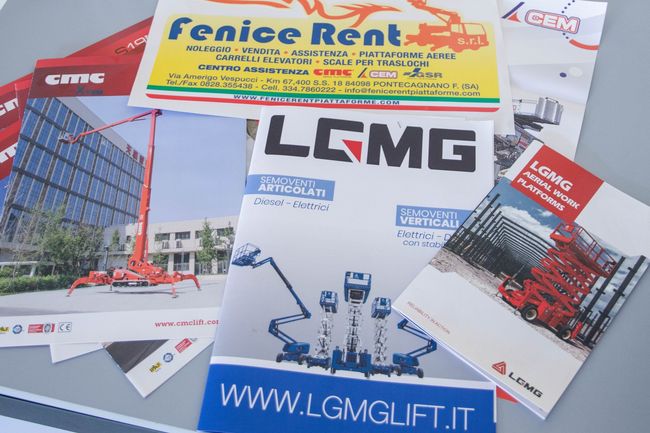 Brochure e adesivi per attrezzature edili, tra cui LGMG e Fenice Rent, su un tavolo.