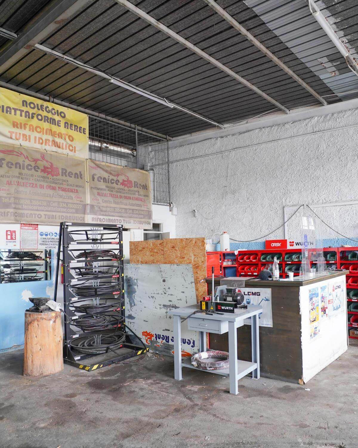 Interno di un'officina: attrezzi, scaffali, un banco da lavoro, casse rosse e insegne sbiadite.
