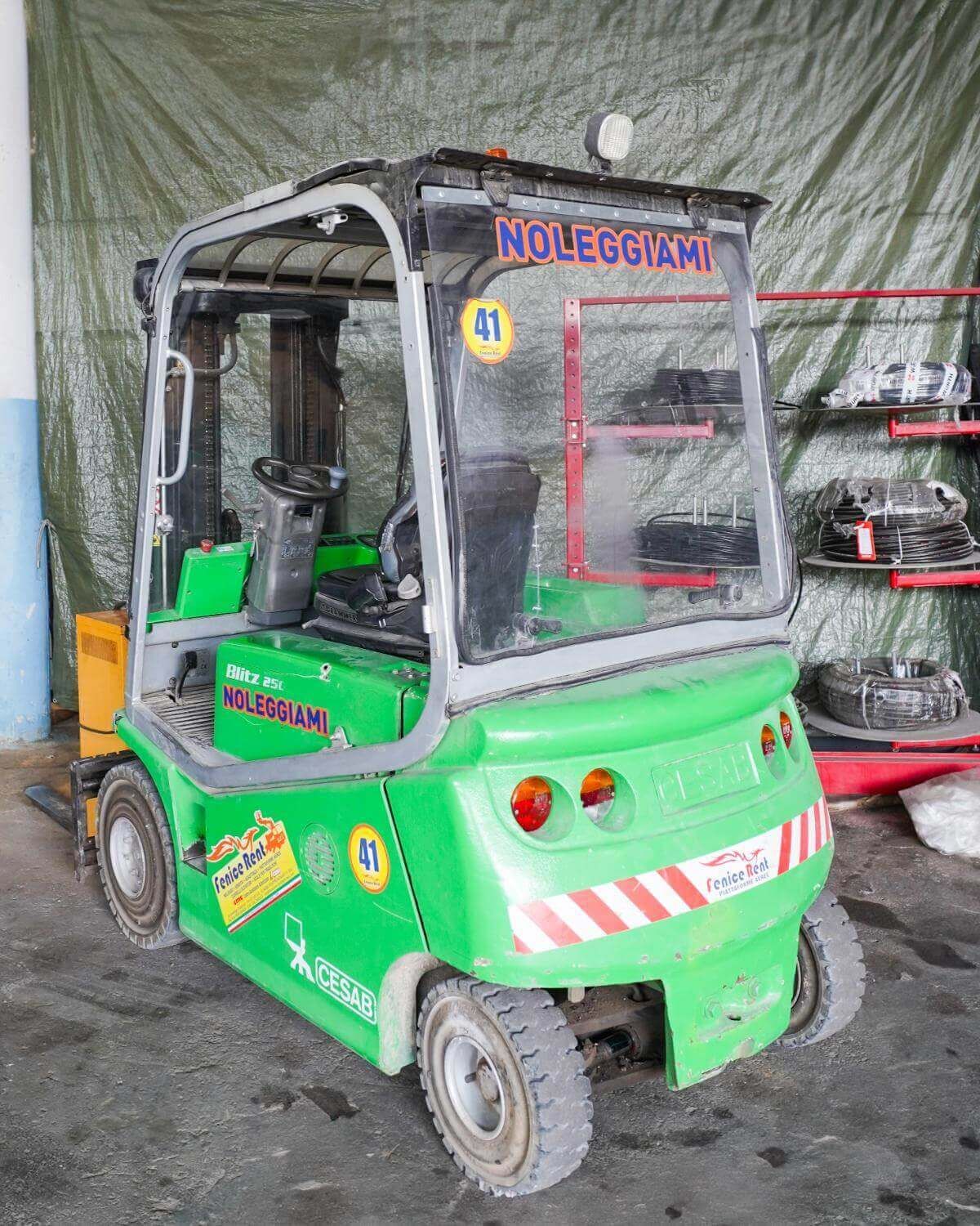 Carrello elevatore verde con cabina, parcheggiato in un magazzino.