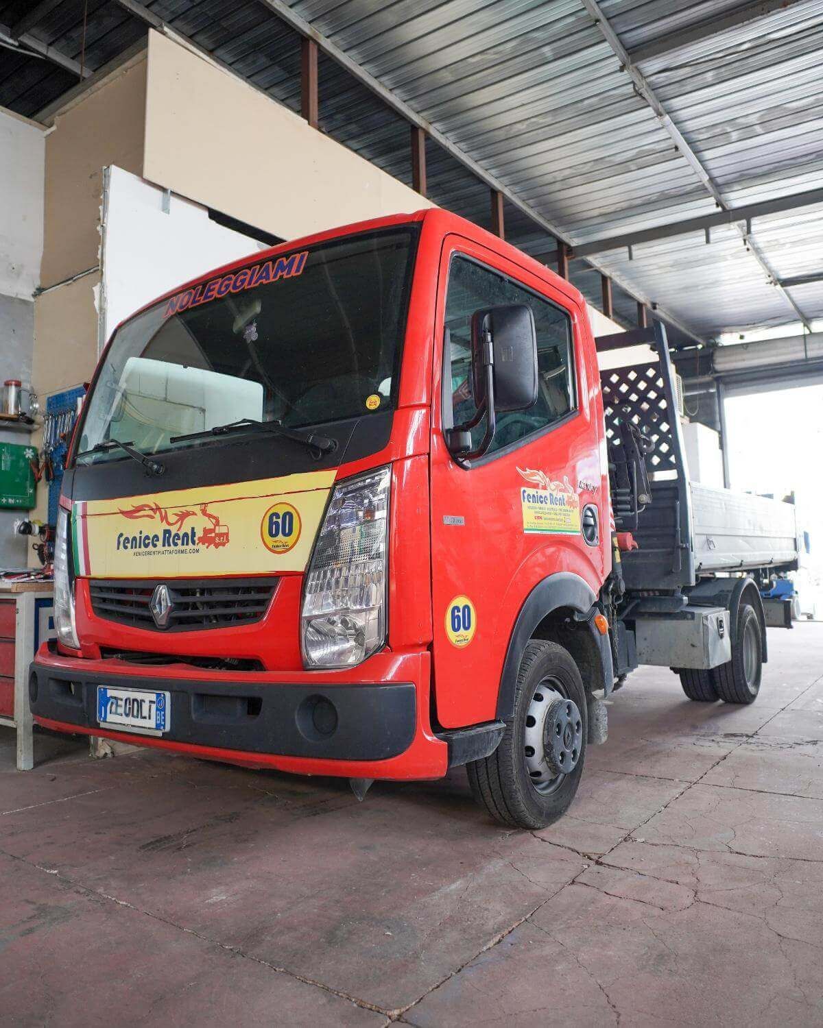 Camion rosso con pianale parcheggiato all'interno di un garage con un cartello che indica il limite di velocità.