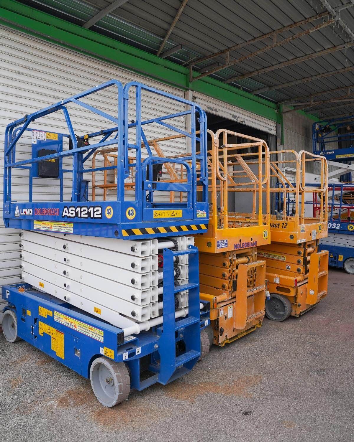 Tre piattaforme aeree, una blu e una gialla, parcheggiate all'interno di un edificio.