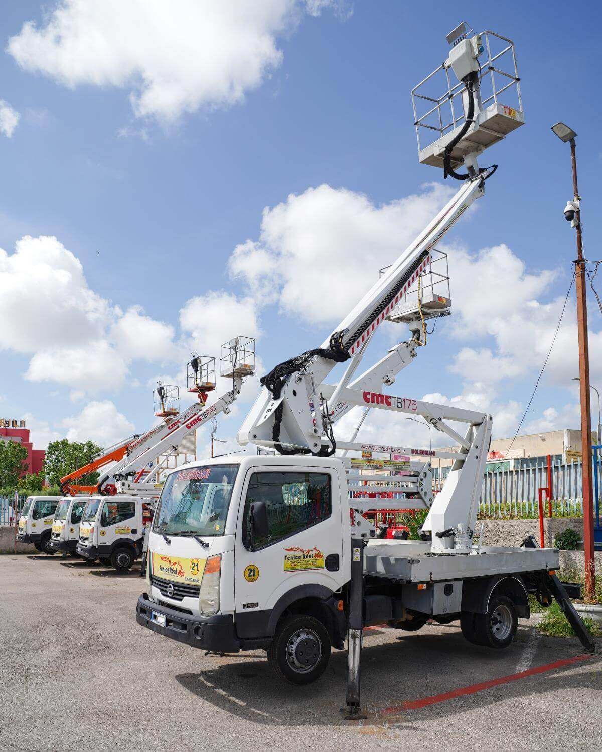 Un camion bianco con piattaforma aerea parcheggiato all'aperto in una giornata di sole. Diversi camion simili sullo sfondo.