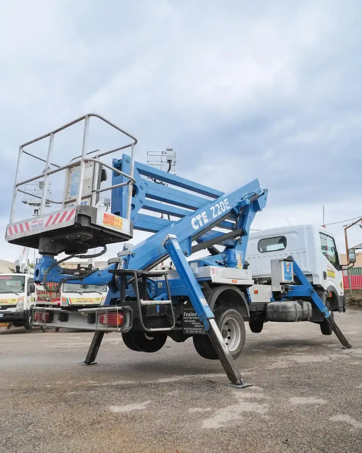 Piattaforma aerea blu montata su un camion con stabilizzatori estesi, pronta per l'uso all'aperto.