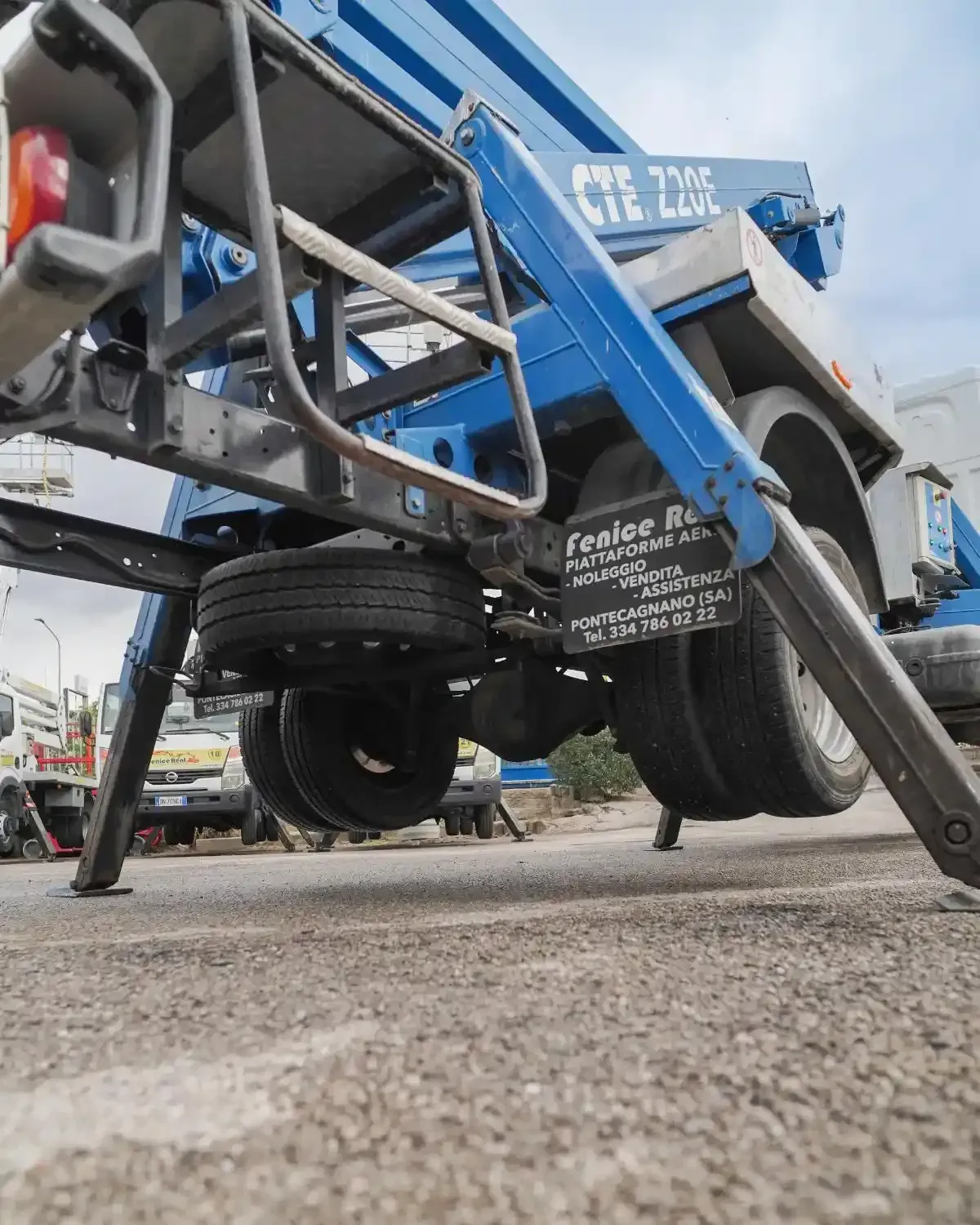 Autocarro elevatore blu su strada con stabilizzatori dispiegati.