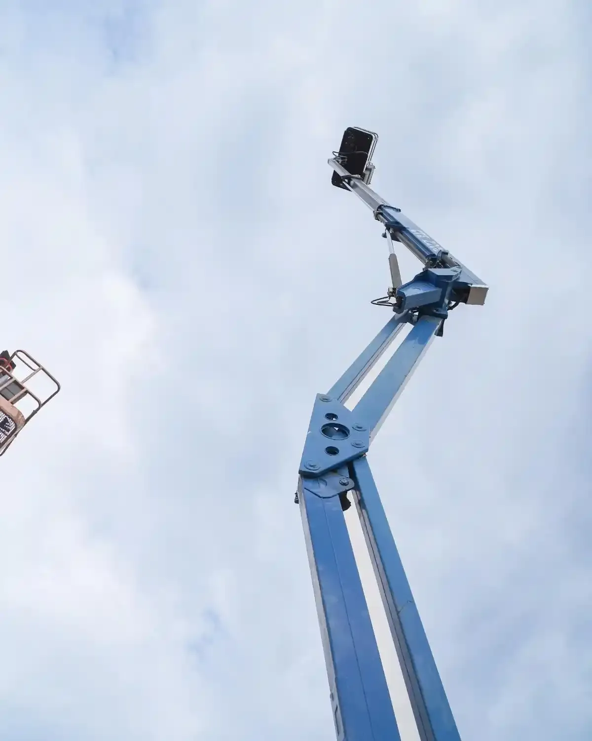 Piattaforma aerea telescopica blu protesa verso l'alto contro un cielo nuvoloso.