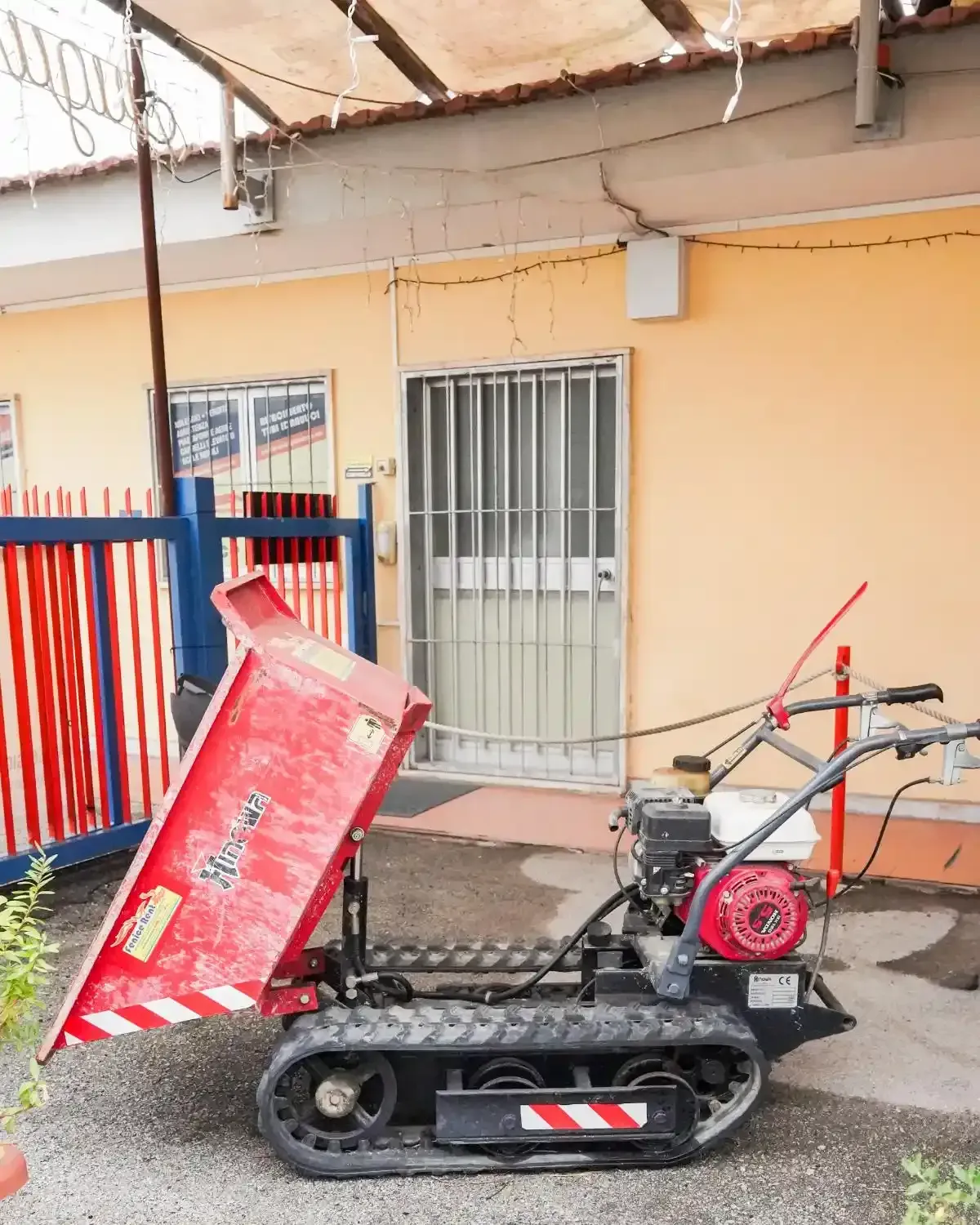 Mini dumper cingolato rosso e nero accanto a un edificio con una porta aperta.
