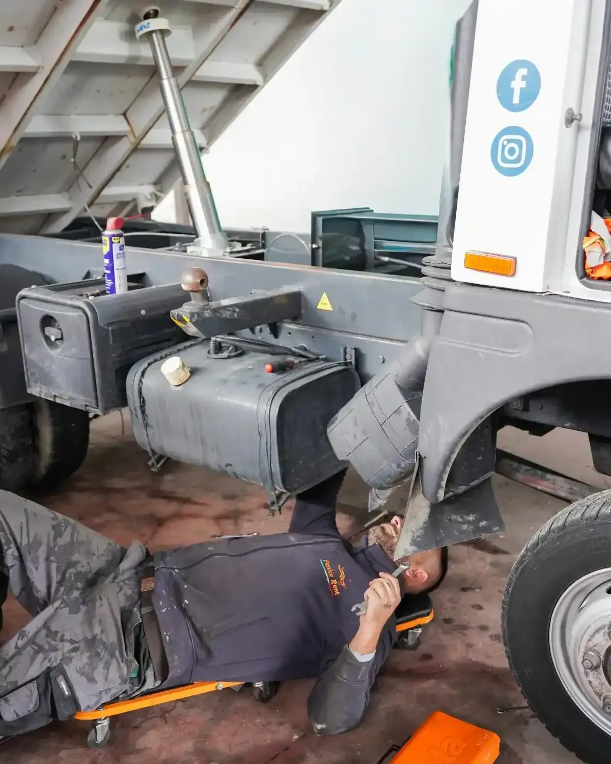 Una persona sdraiata su un carrello elevatore sta lavorando sulla parte inferiore di un camion.