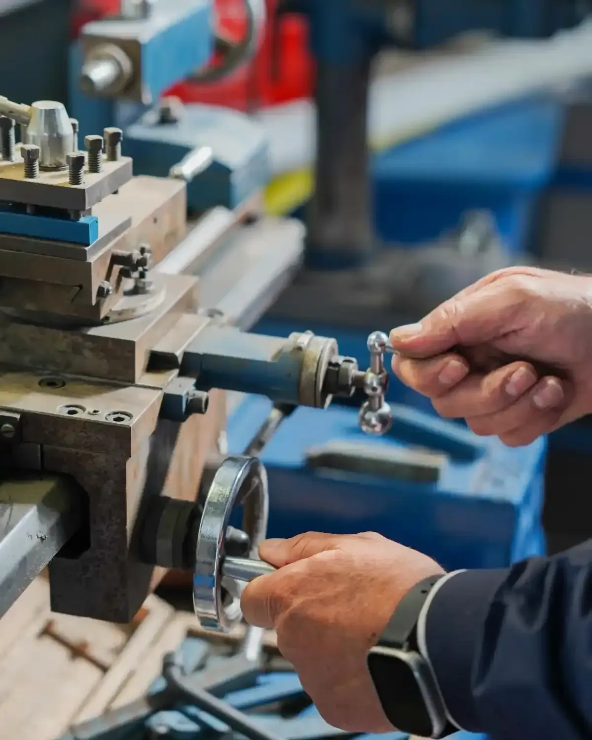 Mani che azionano un tornio per metalli blu in un'officina.