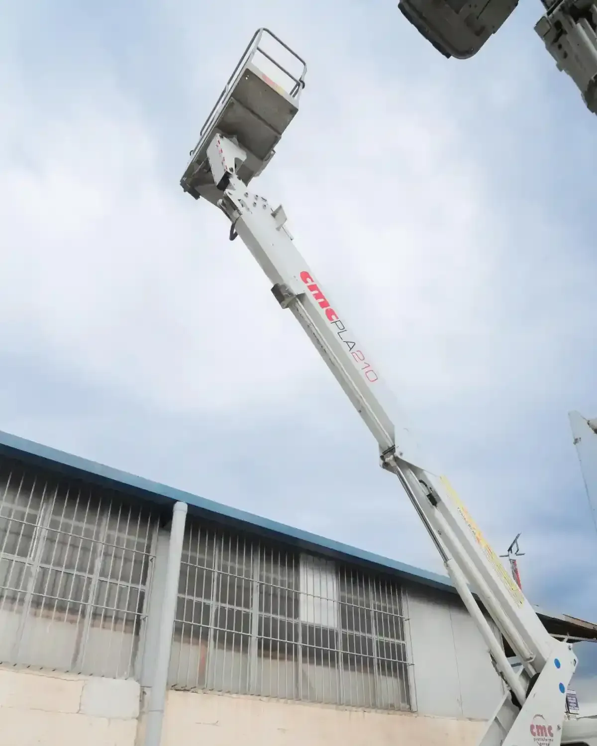 Una piattaforma aerea bianca si estende verso l'alto vicino a un edificio con finestre, sotto un cielo nuvoloso.