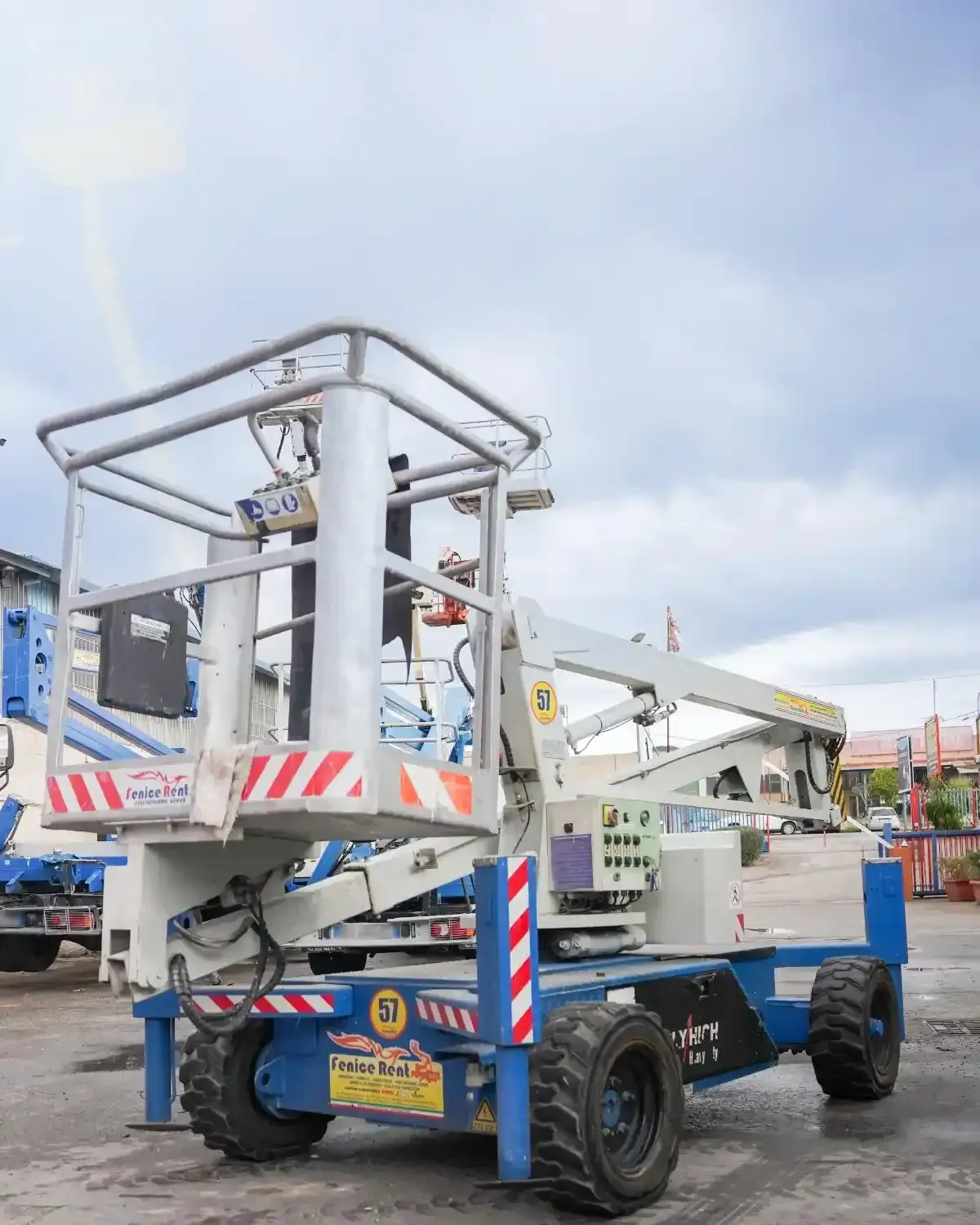 Un mezzo elevatore semovente blu e bianco con piattaforma rialzata, parcheggiato sull'asfalto.