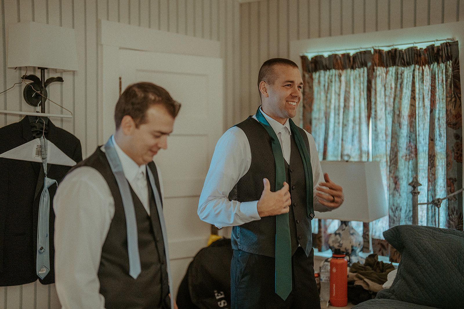 Two men are getting ready for a wedding in a room.