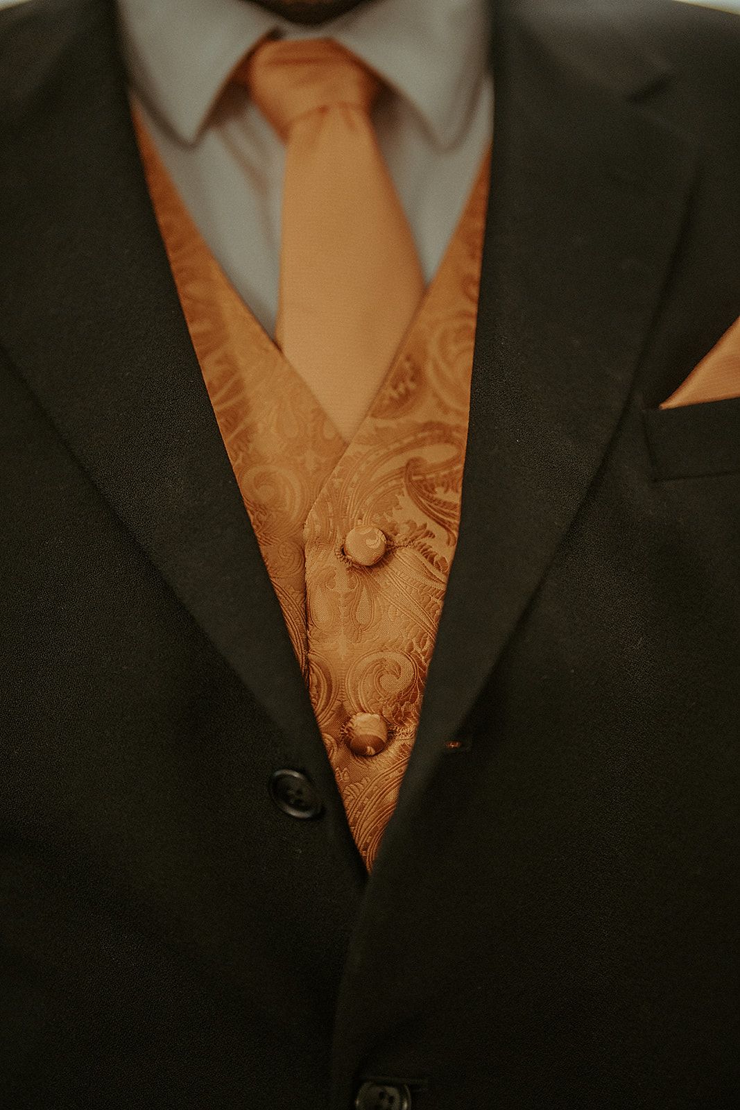 A man in a suit and tie is wearing an orange vest and tie.