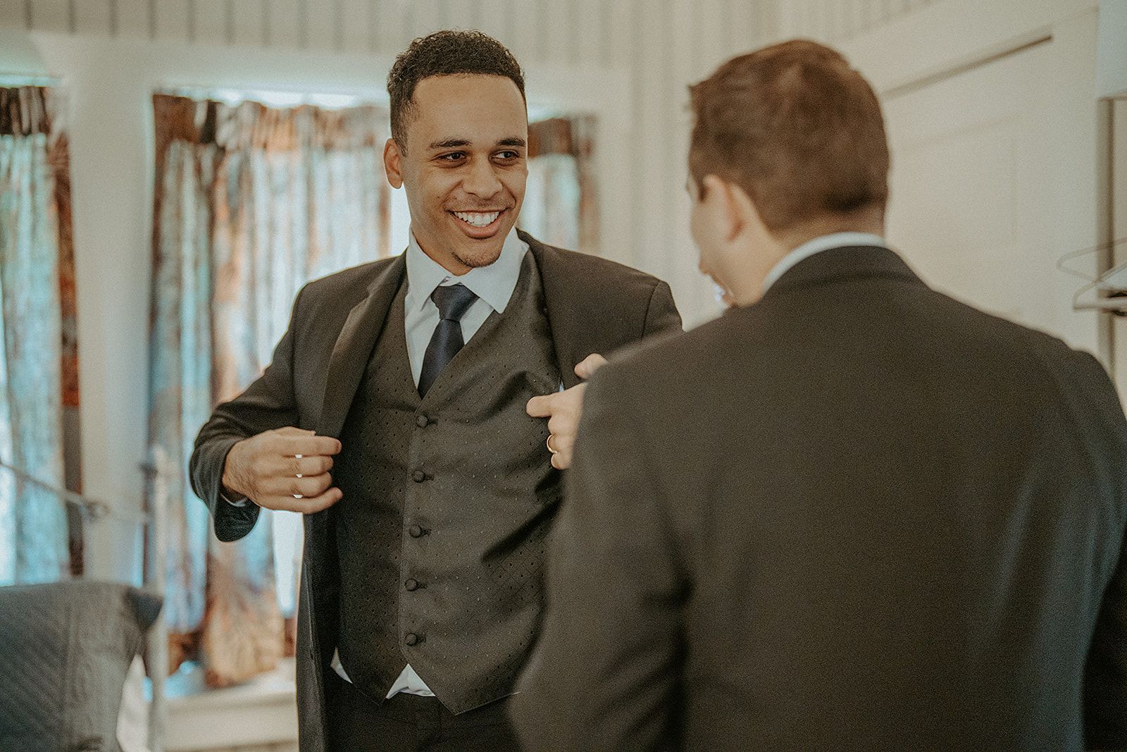 Two men in suits are standing next to each other in front of a mirror.