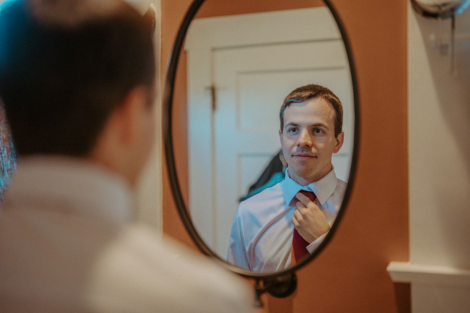 A man is adjusting his tie in front of a mirror.