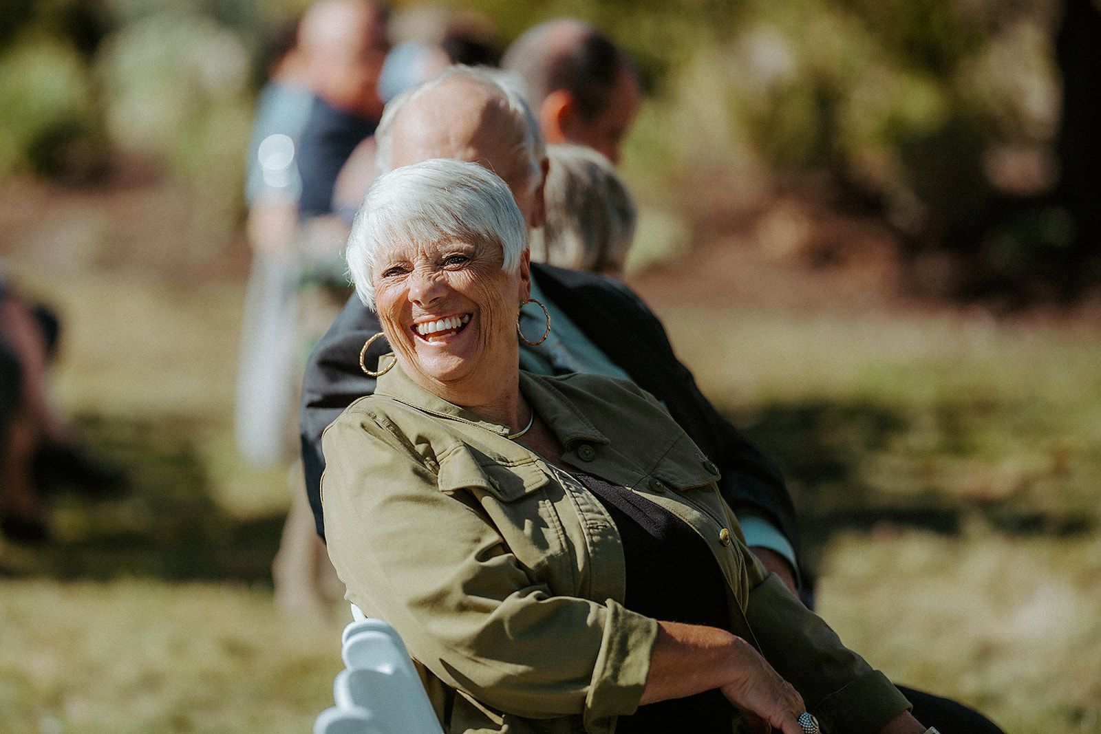 A woman is smiling while sitting in a chair at a wedding.