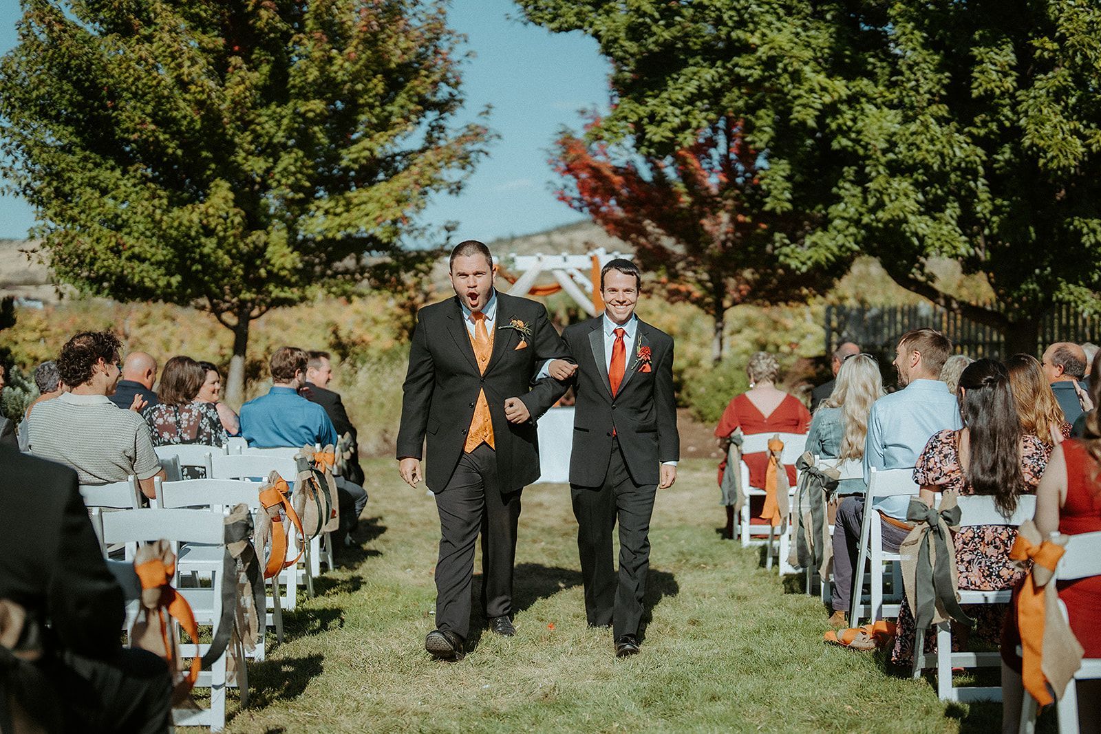 Two groomsmen are walking down the aisle at a wedding ceremony.