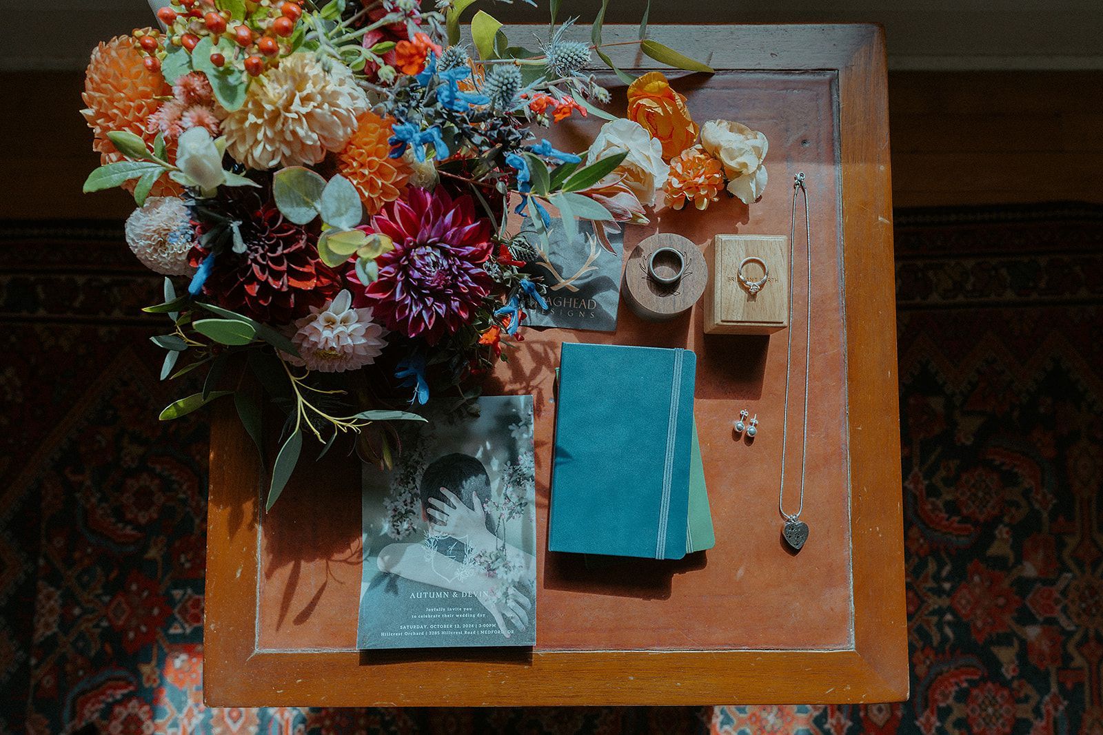 Still life with bouquet, jewelry, ring box, and journal on a wooden table.