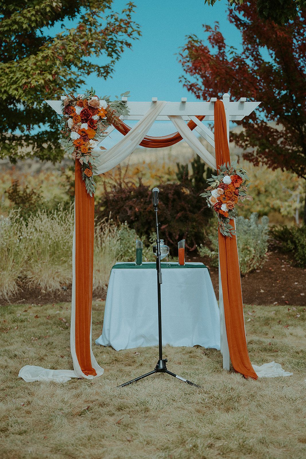 A wedding arch with flowers and a table with a microphone underneath it.